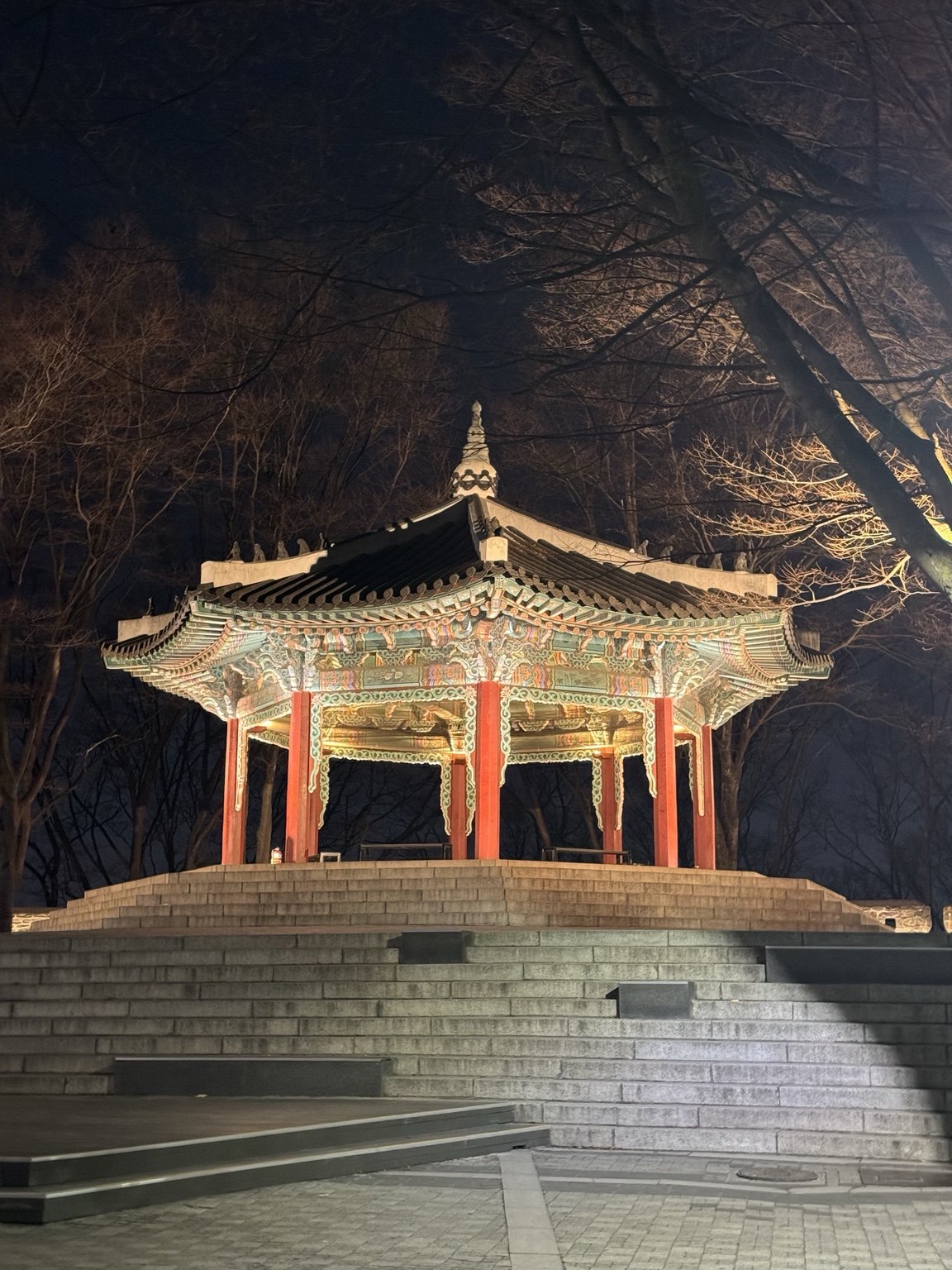 An illuminated Korean pavilion among trees at night