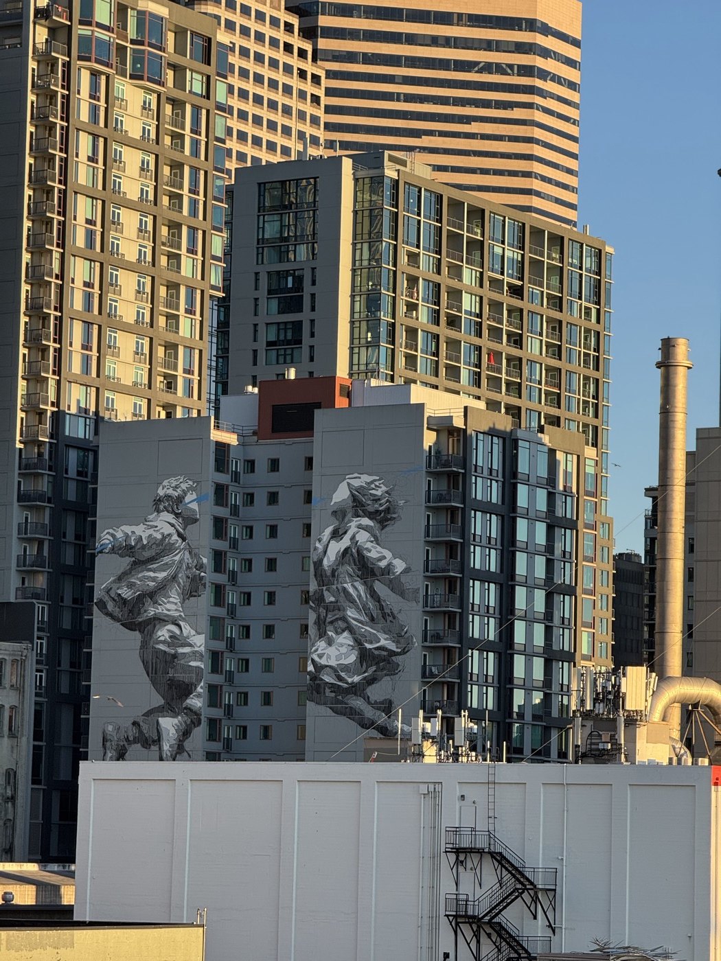 Two large grayscale figures painted on a Seattle building, surrounded by sunlit city towers