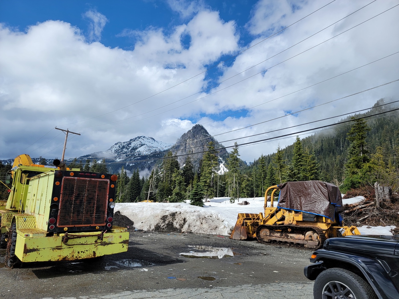 Snow-covered mountains rising behind a roadside work area